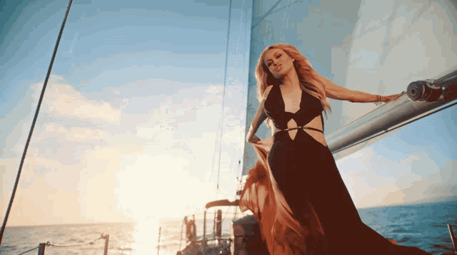 a woman in a long black dress is standing on a sailboat in the ocean