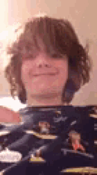 a young boy with curly hair is taking a selfie with a camera while wearing a pajama .