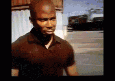 a man in a black shirt is standing in a parking lot and looking at the camera .