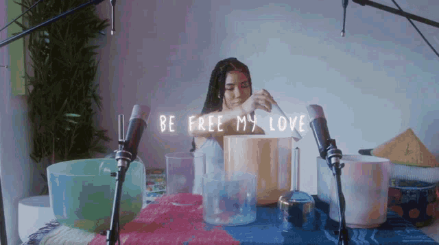 a woman sits at a table with bowls and microphones with the words " be free my love " written above her