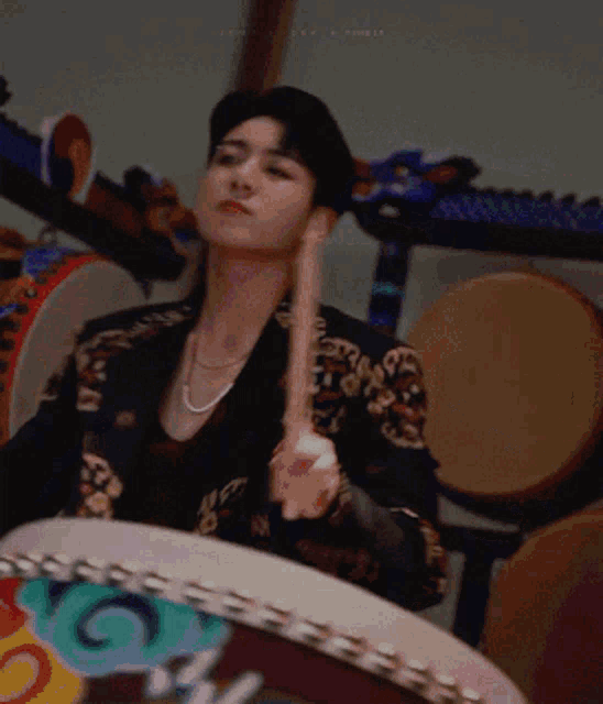 a man in a black jacket is playing a drum with a stick in his hand