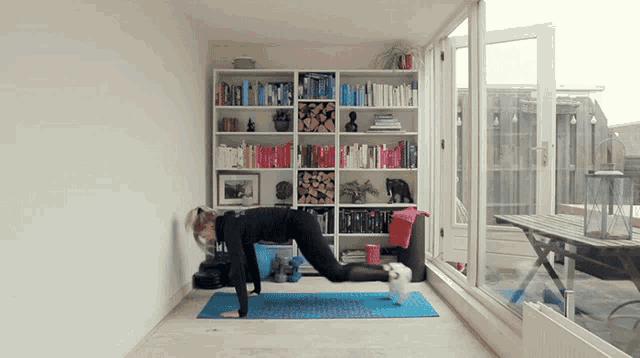 a woman is doing a yoga pose on a blue mat in front of a bookshelf