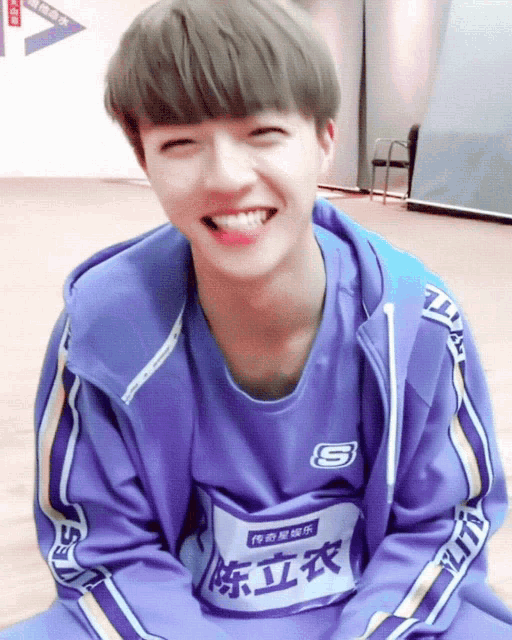 a boy wearing a purple shirt with the letter s on it is smiling