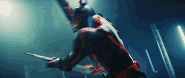 a man in a red and black superhero costume is holding a knife in his hand in a dark room .