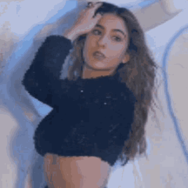 a woman in a black crop top is standing in front of a wall and touching her hair .