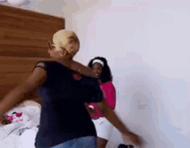 two women are dancing in a bedroom with a wooden headboard in the background .
