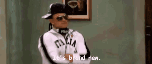 a man wearing a hat and sunglasses is standing in a room and says `` it 's brand new . ''