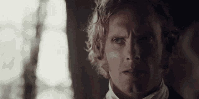 a man with blonde hair and a white shirt is looking at the camera with a serious look on his face .