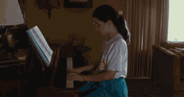 a girl in a white shirt with a smiley face on it plays a piano