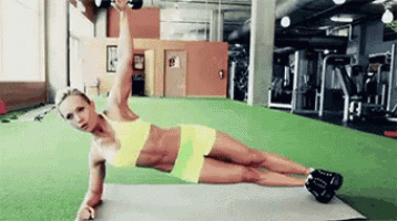 a woman is doing a plank on a mat in a gym while holding a dumbbell over her head .