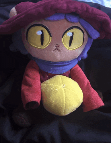 a stuffed animal with a purple hat and yellow eyes is holding a yellow ball