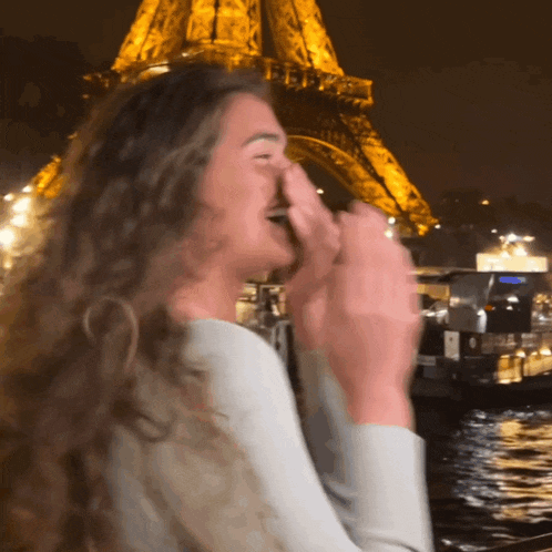 a woman in front of the eiffel tower covering her face with her hands