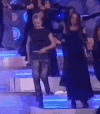 a group of people are dancing on a stage with blue lights behind them .