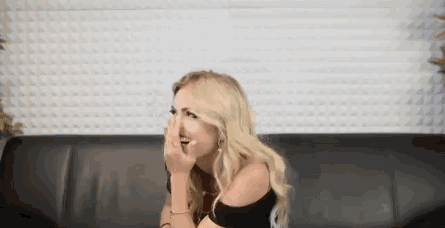 a blonde woman is sitting on a couch covering her nose with her hand .