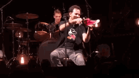 a man is drinking from a red cup while sitting on a stage in front of a drum set .