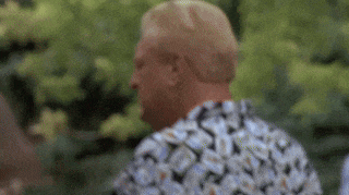 a man wearing a floral shirt is standing in front of a tree .