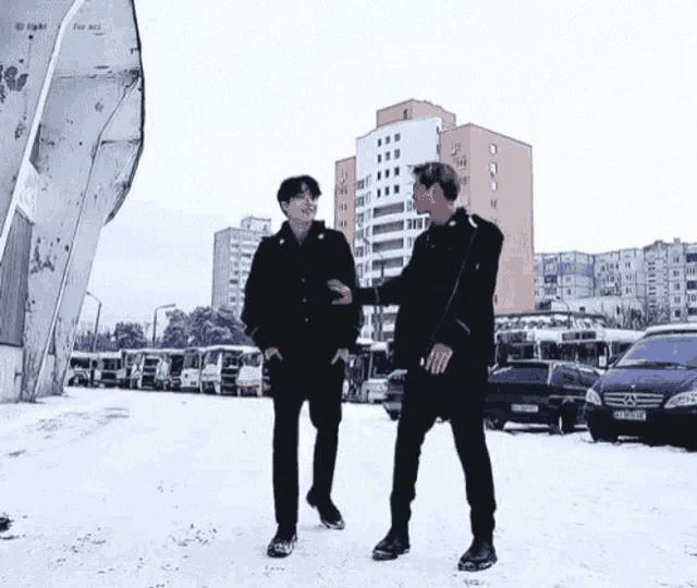 two men are standing in the snow in front of a row of buses .