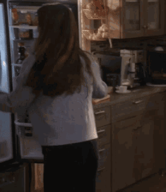 a woman in a white tank top and a blue cardigan is dancing in the kitchen