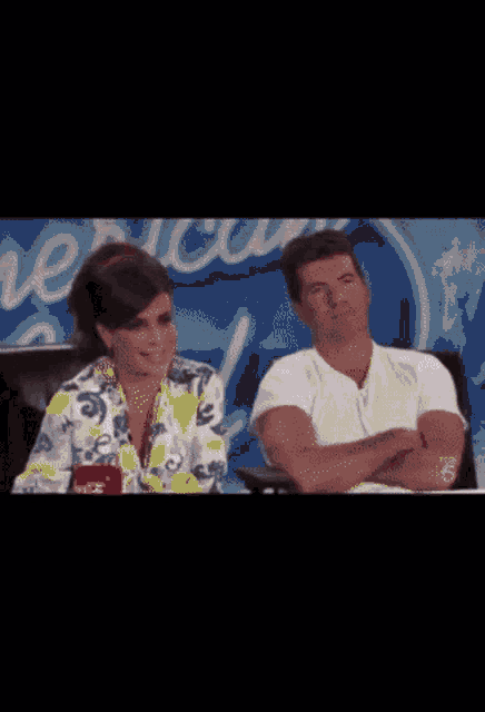 a man and a woman are sitting next to each other in front of an american idol sign