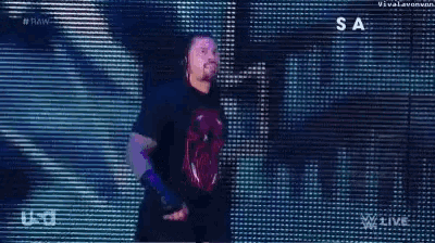roman reigns is walking on a stage in front of a large screen .