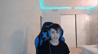 a young man wearing headphones is sitting in a gaming chair in a bedroom .