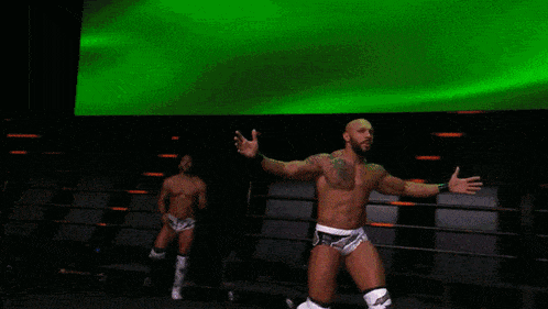 a wrestler with his arms outstretched stands in front of a green screen