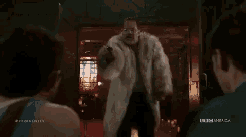 a man in a fur coat is standing in a doorway with a gun .