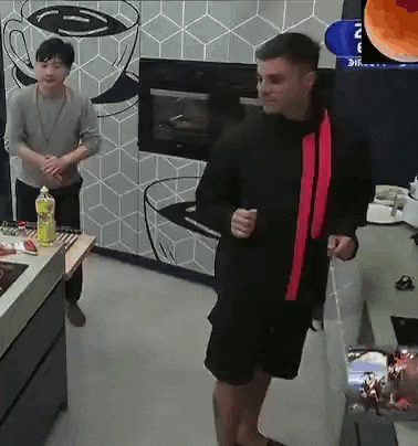a man in a black jacket is standing in a kitchen next to a man in a grey shirt .