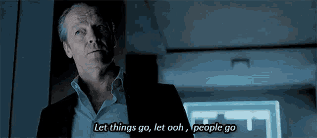 a man in a suit and white shirt is standing in a dark room and saying let things go let ooh people go .