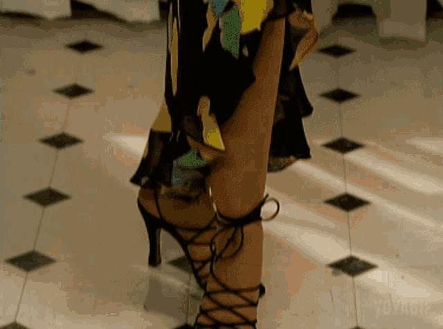 a woman wearing a black dress and black lace up heels stands on a checkered floor