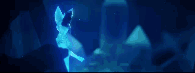 a woman is standing in a cave with a blue light coming out of her chest .
