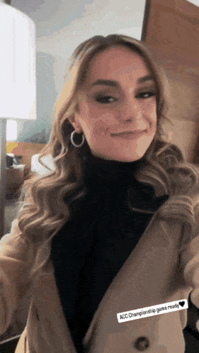 a woman wearing a black turtleneck and a tan coat is smiling