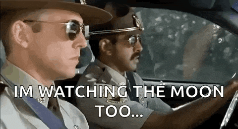 two police officers are driving a car and one of them is watching the moon .