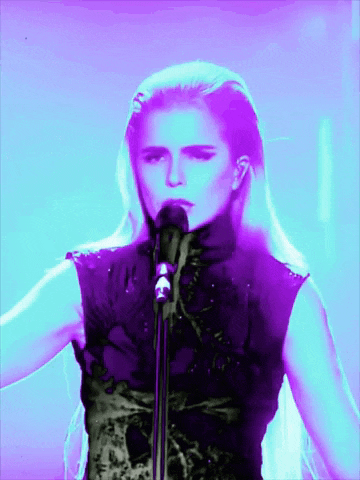 a woman singing into a microphone with purple lights around her