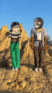 a man and a woman wearing masks are standing on a rocky hill .