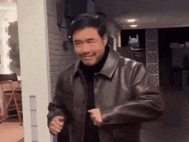 a man in a brown leather jacket is standing in a hallway and smiling