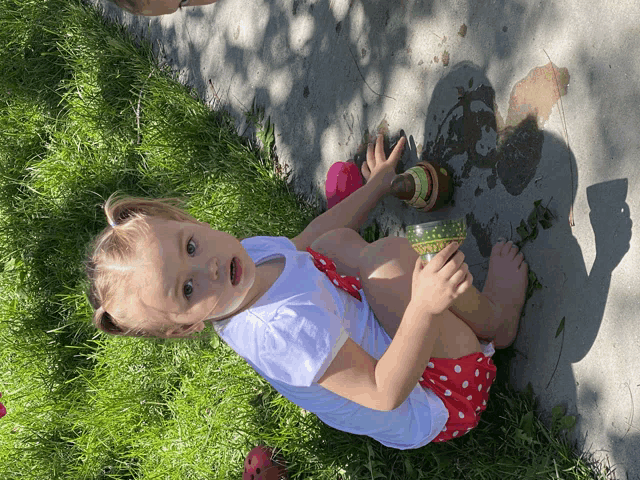 a little girl is sitting on the ground playing with a green container
