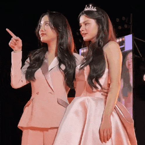 two women are standing next to each other and one is wearing a crown .
