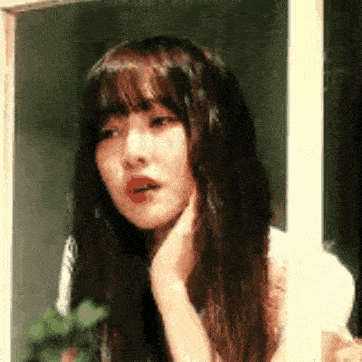 a woman with long hair and bangs is looking out a window .