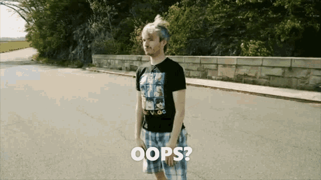 a man in a black shirt and blue shorts is standing on a street and says oops