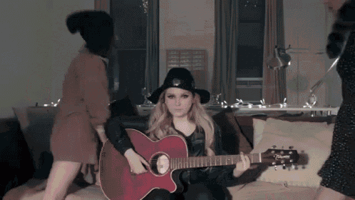 a woman in a black hat is holding a guitar