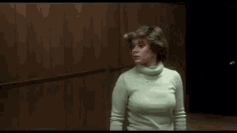 a woman is standing in an elevator wearing a green sweater .
