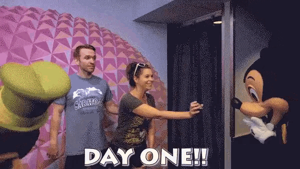 a man and a woman are standing next to a mickey mouse mascot and the words day one on the bottom