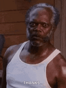 an older man with a beard is wearing a white tank top and looking at the camera .