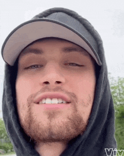 a man with a beard and a hat is wearing a hoodie and a hat .