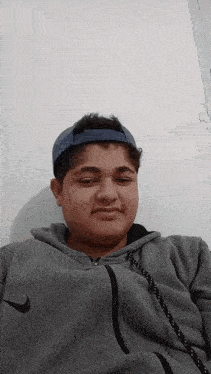 a young man wearing a nike hoodie and a blue hat looks at the camera