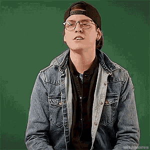 a man wearing glasses and a denim jacket is sitting in front of a green background