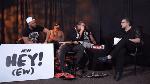 a group of men sitting in front of a sign that says hey