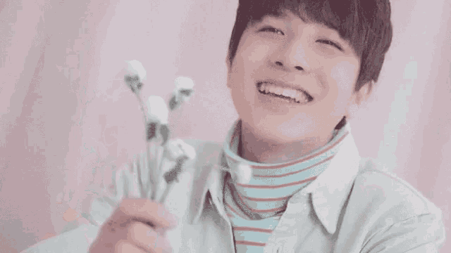 a young man is smiling while holding a bunch of flowers .