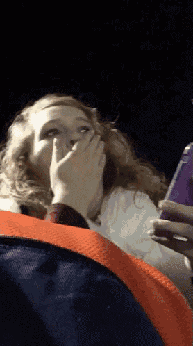 a woman covering her mouth while looking at a cell phone